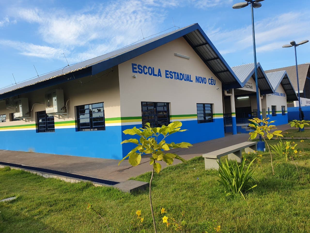 Fachada reformada da escola, com jardim e bancos em primeiro plano